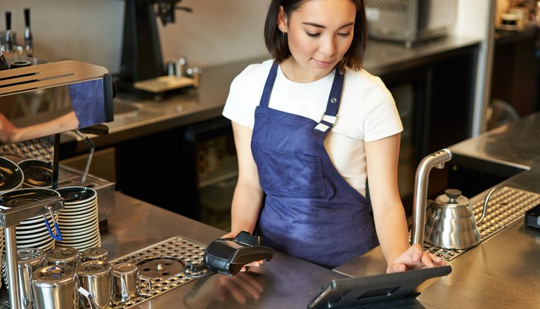 Barista using a point-of-sale terminal at a cafe counter